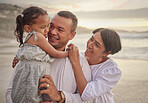 Cute mixed race girl being held outside by her dad and grandmother in the sea at the beach. A young man and his mom holding his cute daughter while standing in the water on the coast at sunset