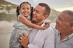 Cute mixed race girl being held outside by her dad and grandfather in the sea at the beach. A young man and his dad holding his cute daughter while standing in the water on the coast at sunset
