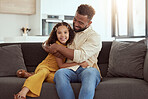 Portrait of mixed race single father and daughter hugging in home living room. Smiling hispanic girl embracing and bonding with single parent in lounge. Happy man and child sitting together on weekend