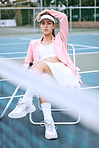 Trendy young tennis player wearing a pink jacket while sitting on chair on a tennis court. Young hispanic sportswoman sitting with a tennis racket after a match