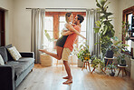 Happy young boyfriend holding girlfriend in arms as he lifts her up while they look into each others eyes and share intimate moment. Romantic young couple hugging and enjoying passionate dance at home