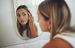 Close up of beautiful young caucasian woman looking in the mirror while touching her face and checking for pimples, wrinkles or bags under eyes during her morning beauty routine