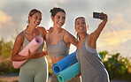 Beautiful yoga women using a cellphone to take selfies while holding yoga mats in outdoor practice in remote nature. Diverse group of young smiling active friends standing together. Three happy people