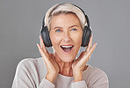 One happy mature woman isolated against a grey background in a studio and wearing headphones to listen to music. Smiling caucasian senior enjoying the loud music and looking youthful and playful