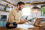 Smiling caucasian man working on laptop in kitchen, checking his email or searching information while doing freelance work at home. Happy young male using internet banking service