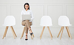 Full length mixed race businesswoman waiting for interview and using laptop. Applicant sitting alone, browsing internet on technology. Candidate in line for job opening, vacancy, office opportunity