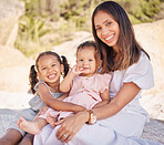 A happy smiling mixed race family of three females only sitting at the beach together. A happy single parent having a picnic with her two little daughters in a park or garden