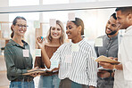 Confident young mixed race businesswoman writing notes and planning a project on a glass wall in an office. Group of smiling businesspeople brainstorming ideas and strategies together in a creative startup agency