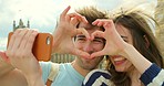 Young couple making a heart with their hands while taking a selfie