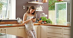 Smiling young woman sending a text message on her cellphone while drinking coffee in her kitchen