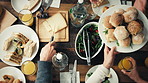 Friends at a party celebrating by eating a meal together. A group of people serving one another lunch at a table from above. Friends eating dinner and drinking together at a party
