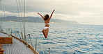 Young woman in a white bikini excitedly jumping off a yacht into the ocean. Woman sailing around Italy jumping off a yacht to swim in the ocean. Woman in white bikini jumping into the sea to swim