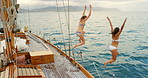 Carefree women in bikinis jumping off a boat into the ocean to swim. Cheerful friends jumping into the ocean from a boat to swim together. Happy women jumping off a boat into the ocean to swim