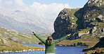 Rear view of a young woman standing with open arms, celebrating life. Unrecognizable woman enjoying the mountain view while hiking through nature on an adventure travel vacation