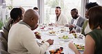 Diverse group of cheerful best friends eating feast and drinking wine while having lunch party around a table in a restaurant or home. Happy men and women socializing with each other over a meal